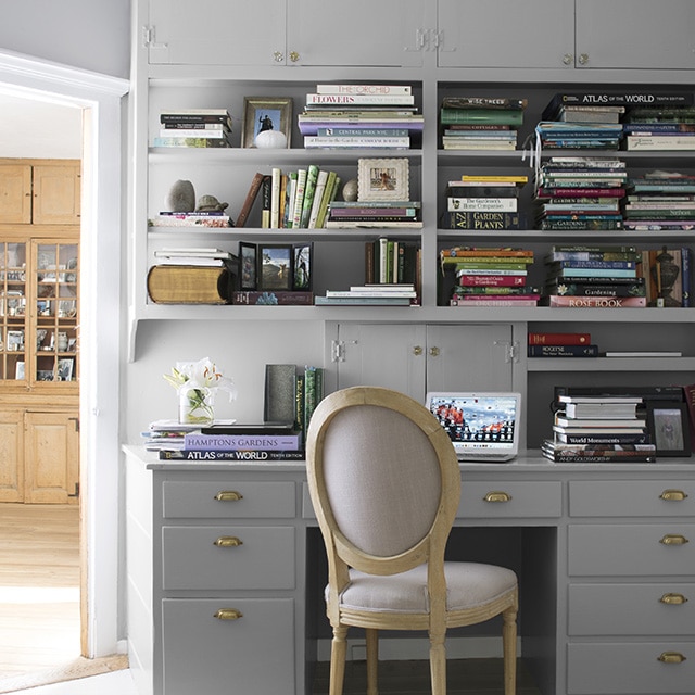 A home office area with built-in gray painted upper cabinets, shelves filled with books, a desk with drawers, a cushioned beige chair, and a pretty star-shaped chandelier. A home office area with built-in gray painted upper cabinets, shelves filled with books, a desk with drawers, a cushioned beige chair, and a pretty star-shaped chandelier.