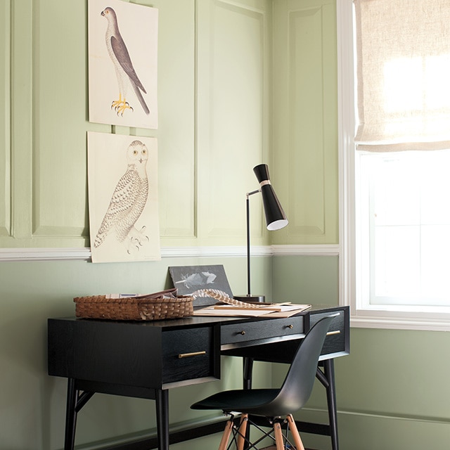 A pretty home office corner space with two-tone green painted walls, wainscoting on the upper walls, a black desk and chair, and bird illustrations. A pretty home office corner space with two-tone green painted walls, wainscoting on the upper walls, a black desk and chair, and bird illustrations.