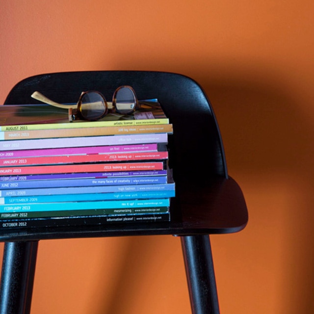 A black chair with a stack of multicolored magazines is set off by an orange wall. A black chair with a stack of multicolored magazines is set off by an orange wall.