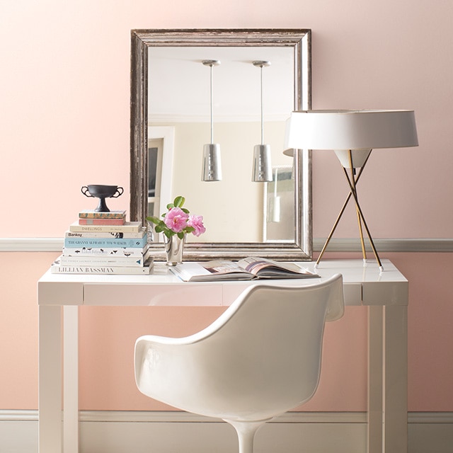 A modern white desk, chair, lamp, and mirror in front of a pretty two-tone pink painted wall with white trim. A modern white desk, chair, lamp, and mirror in front of a pretty two-tone pink painted wall with white trim.