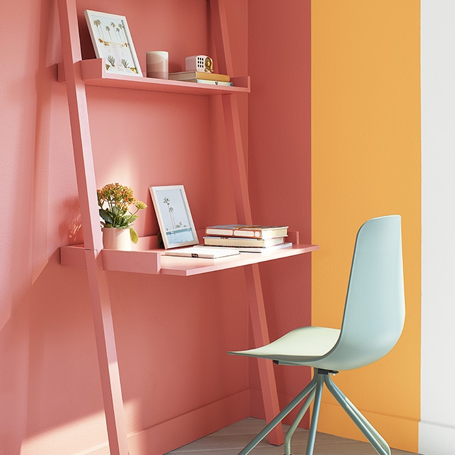 A cheerful corner office space with a large orange rectangle overlapping a golden yellow rectangle painted on white walls, with an orange desk and shelves, and a light green swivel chair. A cheerful corner office space with a large orange rectangle overlapping a golden yellow rectangle painted on white walls, with an orange desk and shelves, and a light green swivel chair.