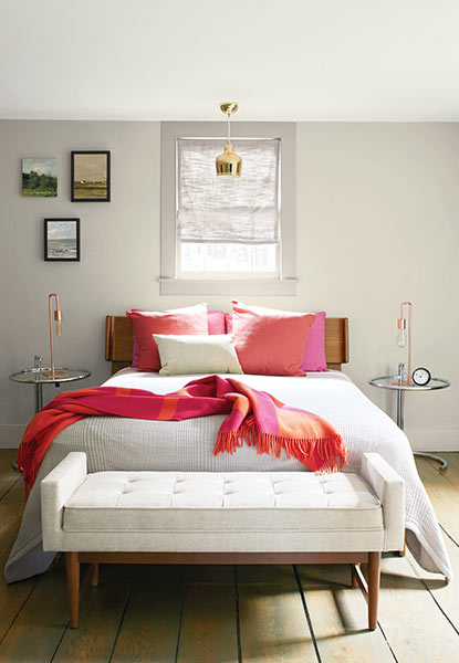 A relaxing bedroom with light gray walls, full size bed with pink pillows and a throw blanket, and cream bench. A relaxing bedroom with light gray walls, full size bed with pink pillows and a throw blanket, and cream bench.