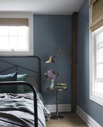 A blue bedroom painted in Black Pepper 2130-40 with exposed wood beams and a black-metal bed frame. A blue bedroom painted in Black Pepper 2130-40 with exposed wood beams and a black-metal bed frame.