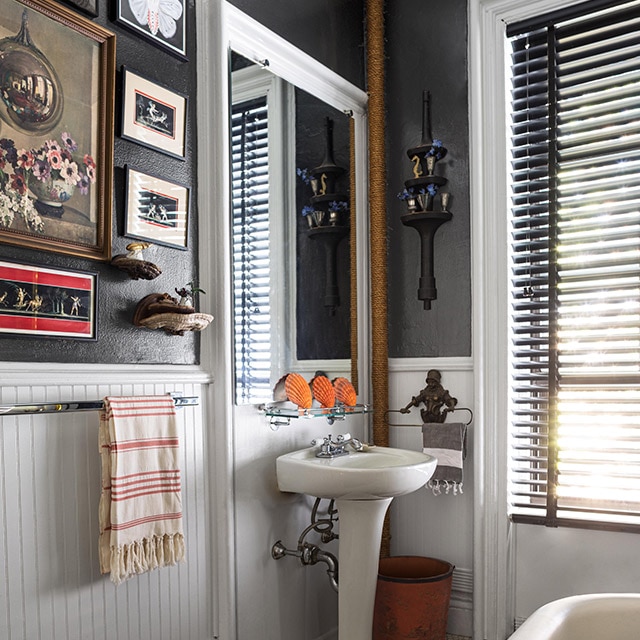 A bathroom with dark gray-painted walls, white wainscoting, trim and ceiling, a pedestal sink and eclectic artwork. A bathroom with dark gray-painted walls, white wainscoting, trim and ceiling, a pedestal sink and eclectic artwork.