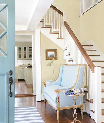 A bright entryway in neutral shades includes a staircase, blue chaise and light blue front door. A bright entryway in neutral shades includes a staircase, blue chaise and light blue front door.