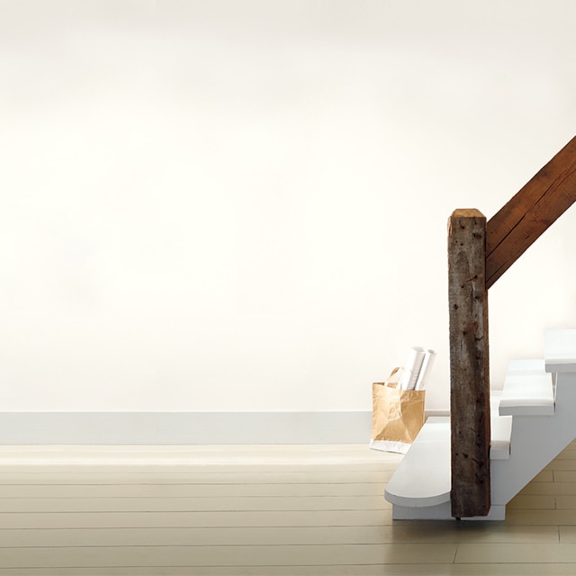A rustic white staircase with wooden handrail in an off-white room; a tote filled with rolled posters sits on the floor.