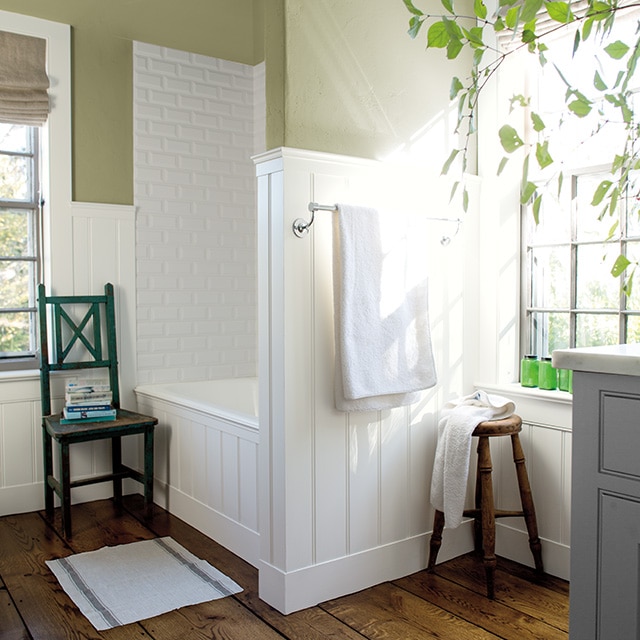 A well-lit bathroom with alcove bath and shower, white wainscoting, beige-painted walls, and wooden seating. A well-lit bathroom with alcove bath and shower, white wainscoting, beige-painted walls, and wooden seating.