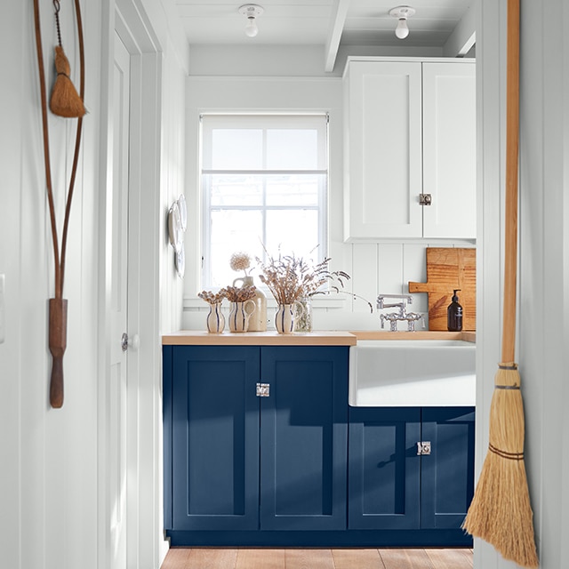 White room with blue counters and wooden top, a large white sink adorned with soap and cutting board, and walls with décor. White room with blue counters and wooden top, a large white sink adorned with soap and cutting board, and walls with décor.