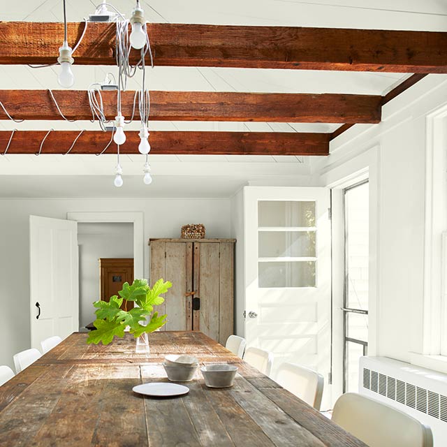 Dining room features a wooden table and white chairs, rustic armoire, wooden counters, and three wooden beams along the ceiling. Dining room features a wooden table and white chairs, rustic armoire, wooden counters, and three wooden beams along the ceiling.
