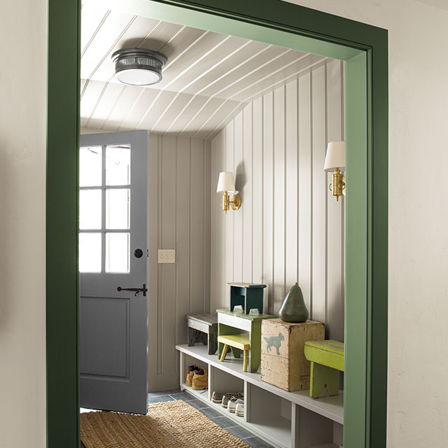 Entryway with white shiplap walls and green trim, featuring wall lighting and cubbyholes with boots. Entryway with white shiplap walls and green trim, featuring wall lighting and cubbyholes with boots.