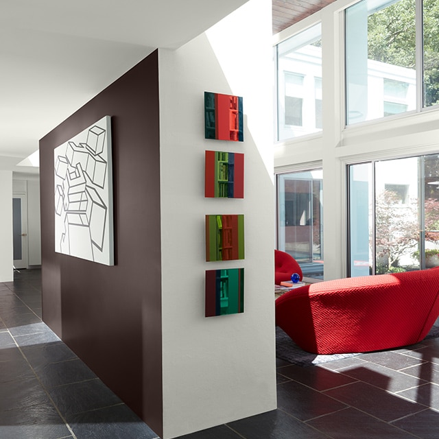 A retro style room with white painted walls and ceiling, a brown accent wall, large windows and a red chair.