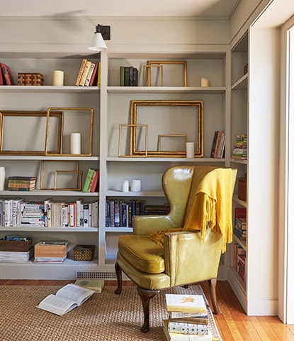 A study with greige-painted walls features alcove bookcases with books and frames, a cozy chair, and golden blanket. A study with greige-painted walls features alcove bookcases with books and frames, a cozy chair, and golden blanket.