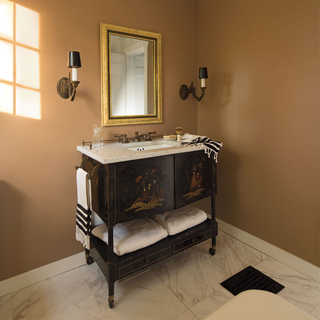 A light orange-painted bathroom with classic sink, gold mirrors, and two wall lights. A light orange-painted bathroom with classic sink, gold mirrors, and two wall lights.