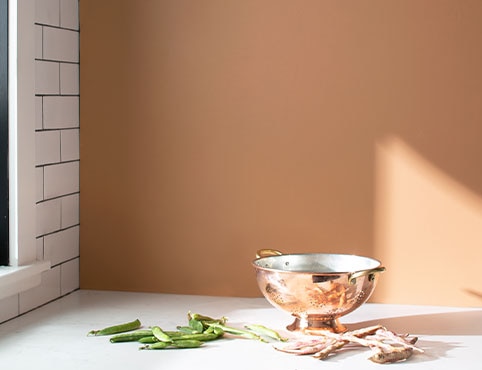 An orange-painted kitchen with a wall of white subway tile, white counters, and copper kitchen instruments. An orange-painted kitchen with a wall of white subway tile, white counters, and copper kitchen instruments.