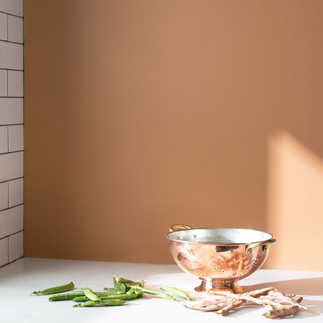 An orange-painted kitchen with a wall of white subway tile, white counters, and copper kitchen instruments.