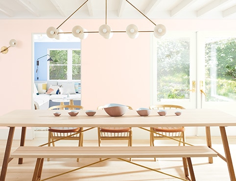 Light pink-painted dining room walls with a long wooden table, matching chairs and bench seating. Light pink-painted dining room walls with a long wooden table, matching chairs and bench seating.