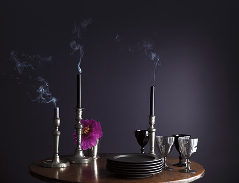 A wooden table with glasses, dishes, and candles in front of a dark purple wall. A wooden table with glasses, dishes, and candles in front of a dark purple wall.