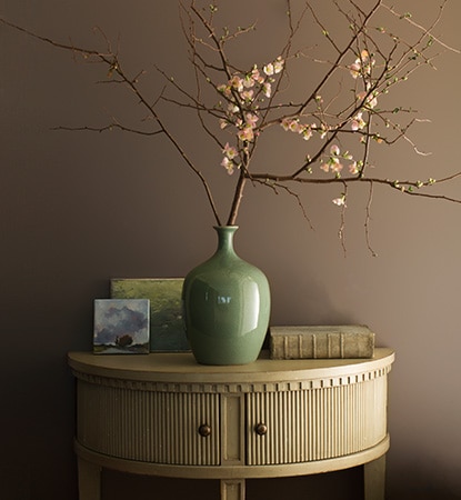 A painted hallway in taupe Weimaraner AF-155 with demi-lune table and jade vase holding flowering branches. A painted hallway in taupe Weimaraner AF-155 with demi-lune table and jade vase holding flowering branches.