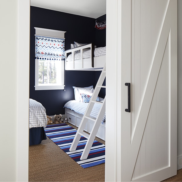 A charming kids bedroom painted in navy blue and white with a bunkbed, striped rug and sliding white barn door. A charming kids bedroom painted in navy blue and white with a bunkbed, striped rug and sliding white barn door.