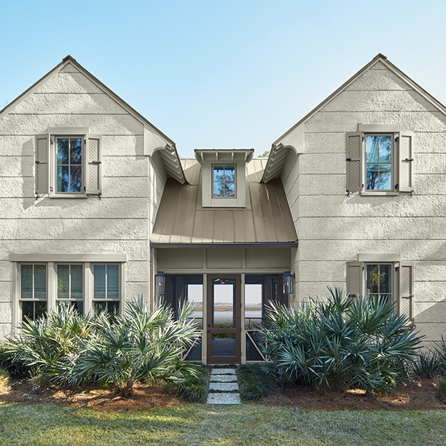 A southern style house painted a stylish off-white with greenish gray undertones, light gray-green shutters and side fence, a brown front door, center breezeway, front greenery and lawn. A southern style house painted a stylish off-white with greenish gray undertones, light gray-green shutters and side fence, a brown front door, center breezeway, front greenery and lawn.