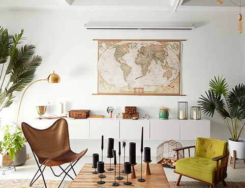 A bright loft living room painted in the same white hue using different sheens with a world map over modern wall-set cabinetry, a leather butterfly chair, a wood cocktail table with black candles, and several planters. A bright loft living room painted in the same white hue using different sheens with a world map over modern wall-set cabinetry, a leather butterfly chair, a wood cocktail table with black candles, and several planters.