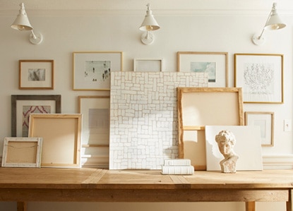 A gallery wall painted in fresh white with a slight pink undertone, a wooden console table styled with art frames and three off-white sconces. A gallery wall painted in fresh white with a slight pink undertone, a wooden console table styled with art frames and three off-white sconces.