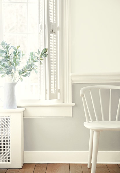 A hallway sitting area in a range of all-white hues with a two-tone painted wall, wall molding, a paned window, white shutters, a white-painted spindle-back chair and wood floor. A hallway sitting area in a range of all-white hues with a two-tone painted wall, wall molding, a paned window, white shutters, a white-painted spindle-back chair and wood floor.