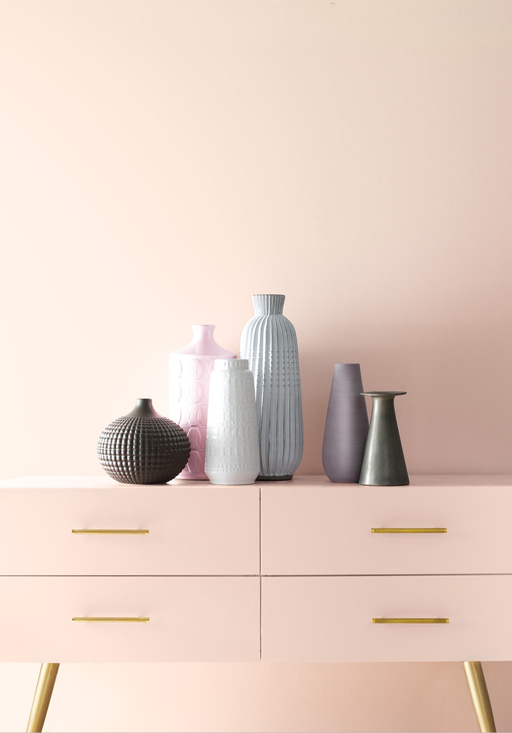 A light pink wall frames a pink console with gold handles and multiple vases