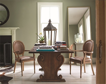 Dark wood table and two chairs in a soft green room with a leaning full length mirror and large window. Dark wood table and two chairs in a soft green room with a leaning full length mirror and large window.