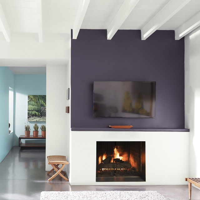 Interior room painted white, with a dark purple accent wall over a fireplace and a blue painted hallway leading out of the room. Interior room painted white, with a dark purple accent wall over a fireplace and a blue painted hallway leading out of the room.