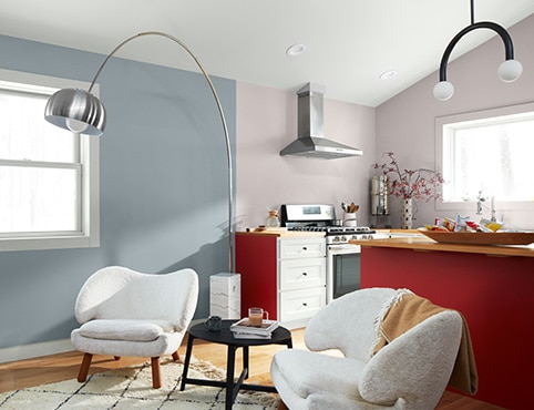 Open living room and kitchen with light blue and lavender-gray walls, a white ceiling, a set of modern white armchairs, and cabinets painted red and white. Open living room and kitchen with light blue and lavender-gray walls, a white ceiling, a set of modern white armchairs, and cabinets painted red and white.