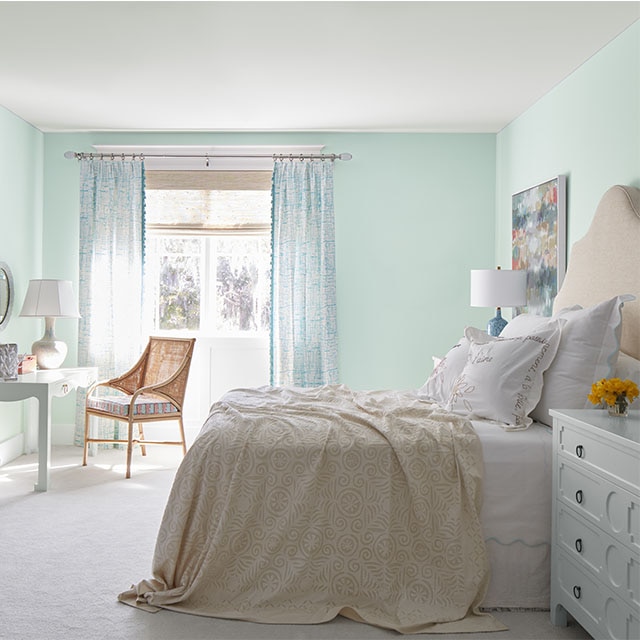 A beachy bedroom painted in a minty green hue with white ceiling, white-painted dresser, and off-white carpeting. A beachy bedroom painted in a minty green hue with white ceiling, white-painted dresser, and off-white carpeting.
