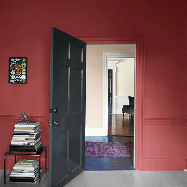 A pomegranate-colored wall with an open dark gray-painted door and table with books. A pomegranate-colored wall with an open dark gray-painted door and table with books.