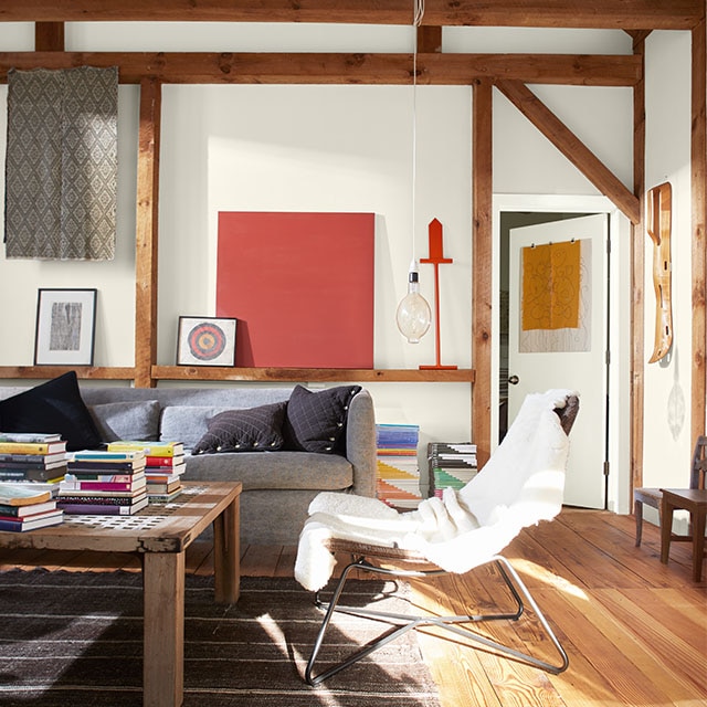 Exterior light streams into an inviting living room painted in white hues, exposed wood beams, gray couch, wood floor, and pops of color throughout. Exterior light streams into an inviting living room painted in white hues, exposed wood beams, gray couch, wood floor, and pops of color throughout.