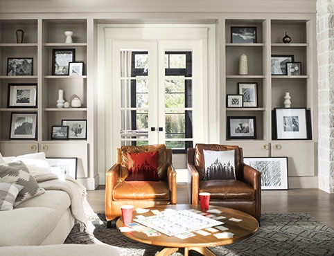 A comfy living room with gray-painted built-in bookshelves, white French doors, a white sofa, and brown leather chairs. A comfy living room with gray-painted built-in bookshelves, white French doors, a white sofa, and brown leather chairs.