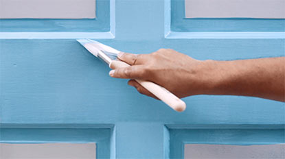 A person brushing blue paint onto a door. A person brushing blue paint onto a door.