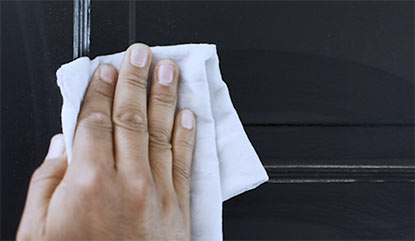 A person cleaning a black door with a white cloth. A person cleaning a black door with a white cloth.