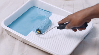 A person rolling blue paint in a paint tray. A person rolling blue paint in a paint tray.