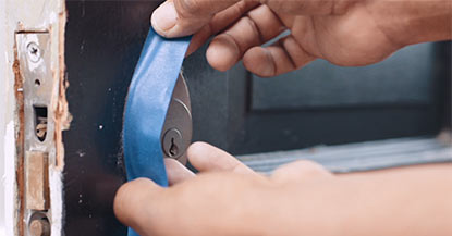 A person applying painter’s tape around a door deadbolt. A person applying painter’s tape around a door deadbolt.