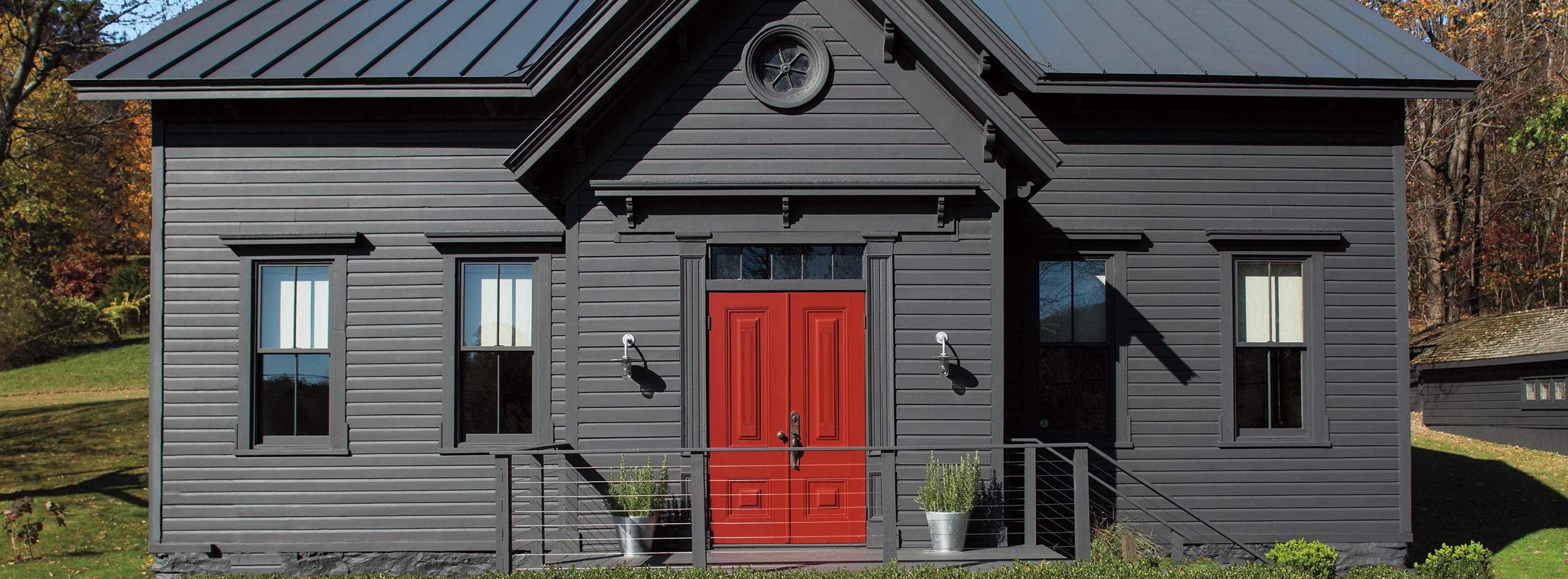 A home with a dark red-painted front door adds a pop of color to a gray-black-painted exterior. A home with a dark red-painted front door adds a pop of color to a gray-black-painted exterior.