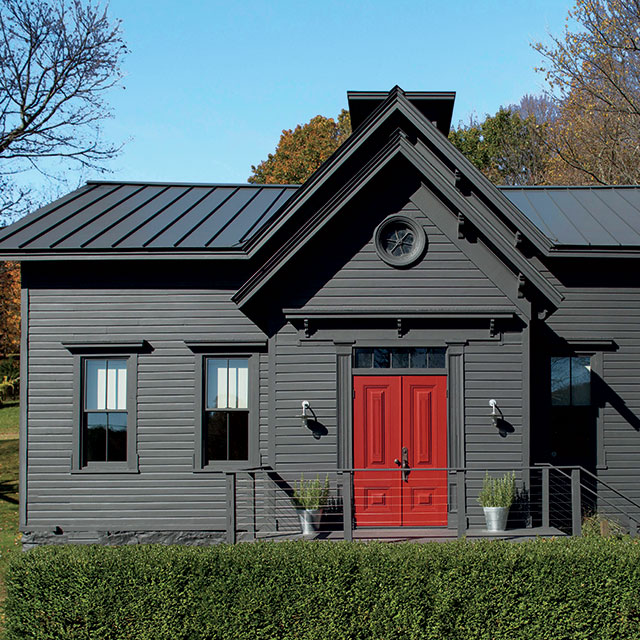 A home with a dark red-painted front door adds a pop of color to a gray-black-painted exterior. A home with a dark red-painted front door adds a pop of color to a gray-black-painted exterior.