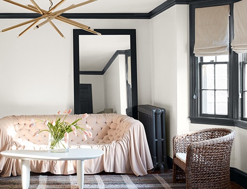 A white-painted living room with black trim and a black-painted radiator, a pink sofa, plaid rug, and modern chandelier. A white-painted living room with black trim and a black-painted radiator, a pink sofa, plaid rug, and modern chandelier.