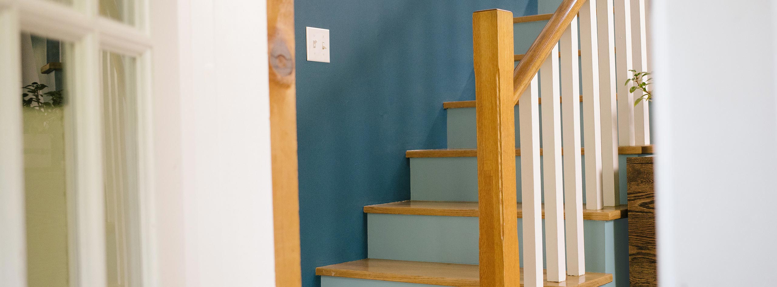 A staircase with blue wall, light blue risers, white balusters, and natural wooden treads and handrails. A staircase with blue wall, light blue risers, white balusters, and natural wooden treads and handrails.
