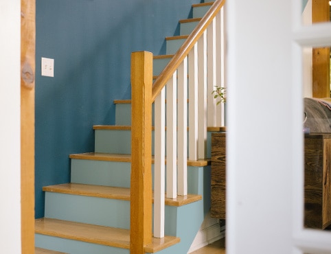 A staircase with blue wall, light blue risers, white balusters, and natural wooden treads and handrails. A staircase with blue wall, light blue risers, white balusters, and natural wooden treads and handrails.
