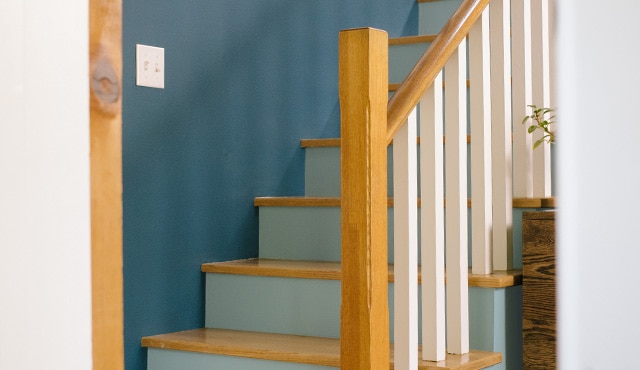 A staircase with blue wall, light blue risers, white balusters, and natural wooden treads and handrails. A staircase with blue wall, light blue risers, white balusters, and natural wooden treads and handrails.