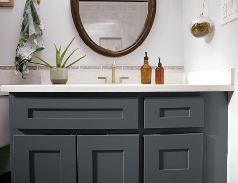 A close-up of a dark bathroom vanity cabinet, white countertops, muted pink tiles backsplash, and one indoor plant. A close-up of a dark bathroom vanity cabinet, white countertops, muted pink tiles backsplash, and one indoor plant.