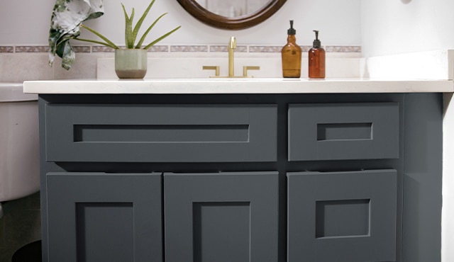 A close-up of a dark bathroom vanity cabinet, white countertops, muted pink tiles backsplash, and one indoor plant. A close-up of a dark bathroom vanity cabinet, white countertops, muted pink tiles backsplash, and one indoor plant.