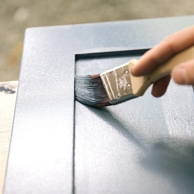 A homeowner painting bathroom cabinets using a paintbrush and ADVANCE Interior Paint. A homeowner painting bathroom cabinets using a paintbrush and ADVANCE Interior Paint.