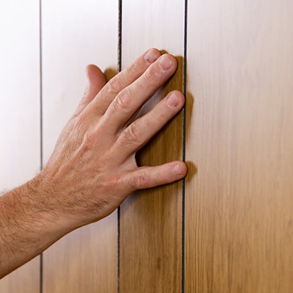 A homeowner touches wood paneling to determine the type. A homeowner touches wood paneling to determine the type.