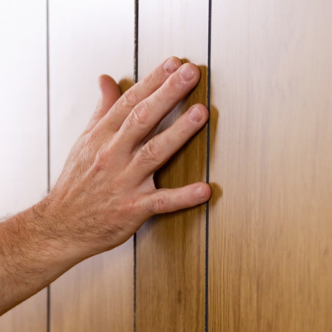 A homeowner touches wood paneling to determine the type. A homeowner touches wood paneling to determine the type.